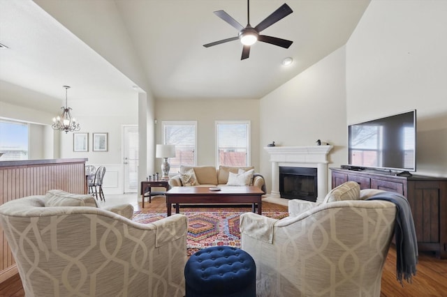 living area featuring a fireplace with raised hearth, high vaulted ceiling, a wainscoted wall, wood finished floors, and a ceiling fan