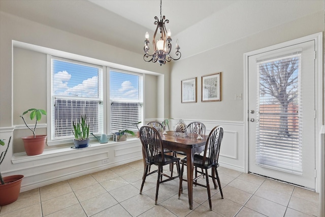 dining room with a wainscoted wall, light tile patterned flooring, a notable chandelier, and a decorative wall