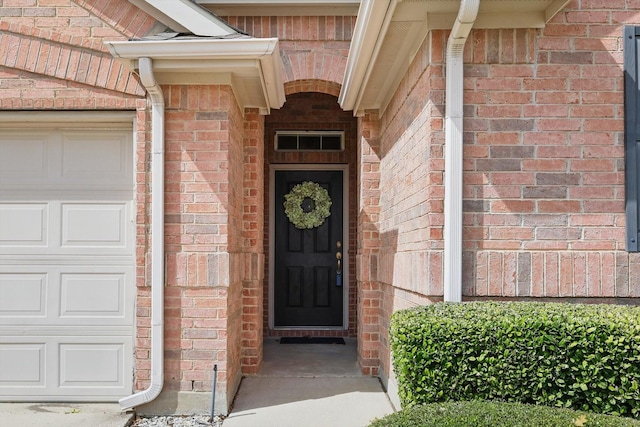 view of exterior entry with a garage and brick siding