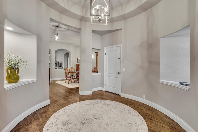 foyer entrance featuring dark wood-style floors, baseboards, arched walkways, and an inviting chandelier