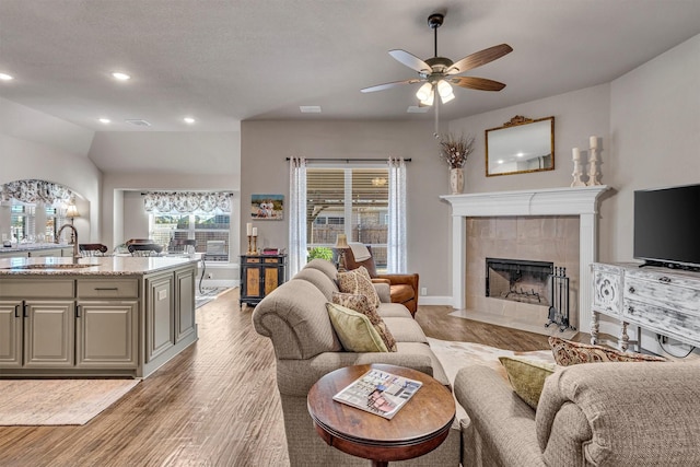 living area with baseboards, a tiled fireplace, ceiling fan, light wood-style floors, and recessed lighting