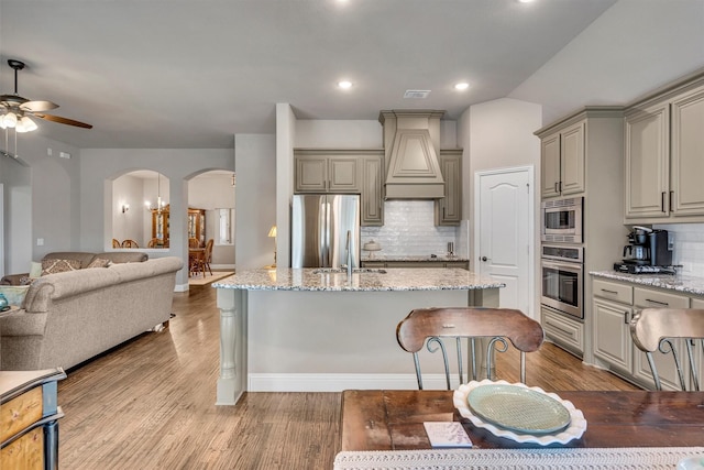 kitchen featuring arched walkways, stainless steel appliances, gray cabinets, custom range hood, and open floor plan