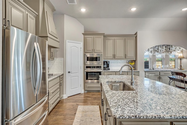 kitchen featuring a center island with sink, appliances with stainless steel finishes, wood finished floors, cream cabinets, and a sink