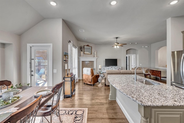 kitchen with arched walkways, a ceiling fan, light stone countertops, light wood-style floors, and a sink