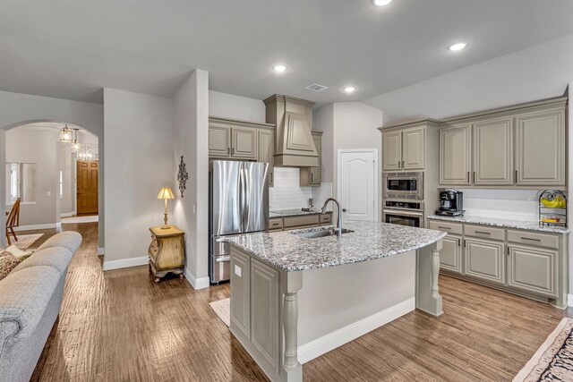 kitchen featuring arched walkways, custom range hood, appliances with stainless steel finishes, light wood-style floors, and a sink