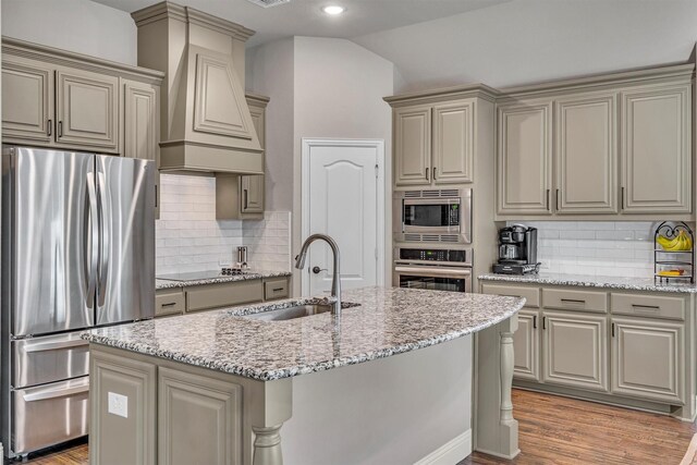 kitchen featuring lofted ceiling, cream cabinets, stainless steel appliances, premium range hood, and a sink