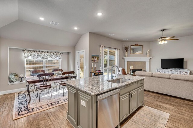 kitchen with light wood finished floors, a tiled fireplace, dishwasher, an island with sink, and a sink