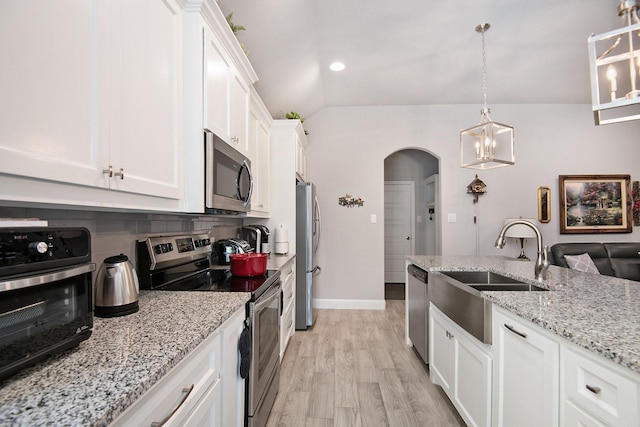 kitchen with arched walkways, stainless steel appliances, a sink, white cabinets, and tasteful backsplash