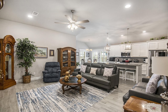 living room featuring lofted ceiling, visible vents, light wood-style flooring, and ceiling fan with notable chandelier