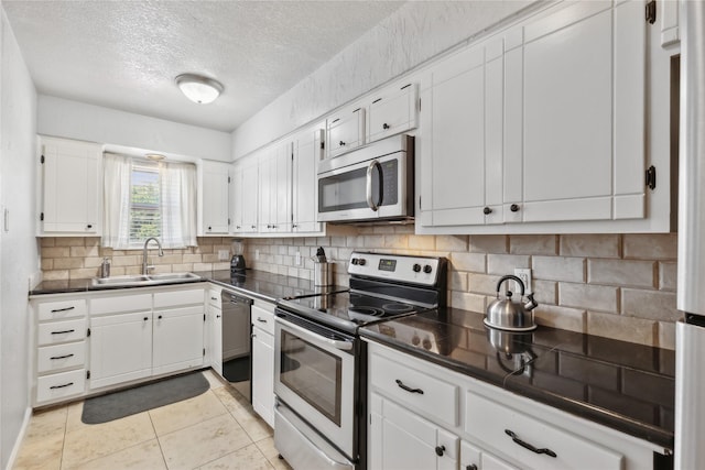kitchen with white cabinets, stainless steel appliances, dark countertops, a sink, and backsplash