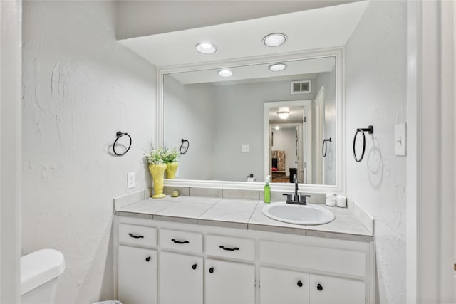 half bath featuring toilet, vanity, a textured wall, and visible vents