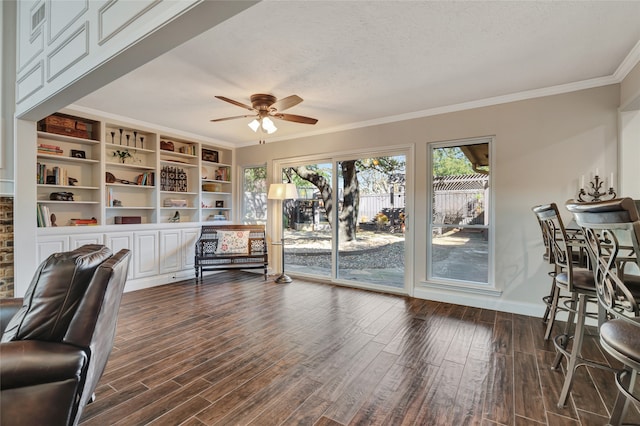 interior space with a textured ceiling, dark wood-type flooring, a ceiling fan, baseboards, and ornamental molding