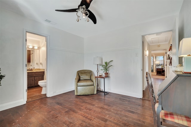 sitting room with attic access, dark wood-style flooring, visible vents, and wainscoting