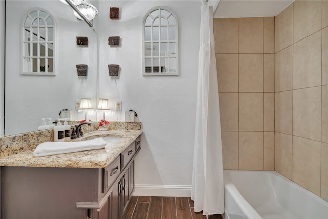 full bath featuring a textured wall, shower / bath combo, vanity, wood finished floors, and baseboards