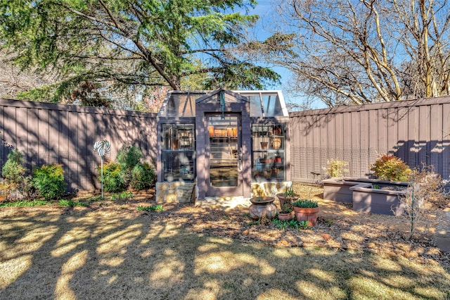 view of yard with a garden, a greenhouse, a fenced backyard, and an outdoor structure