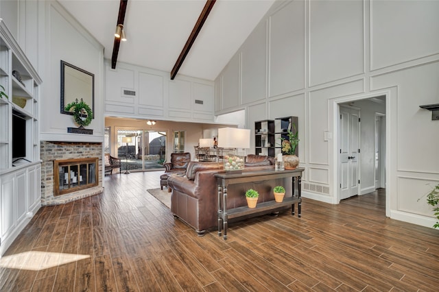 living area with visible vents, beamed ceiling, wood finished floors, a fireplace, and a decorative wall