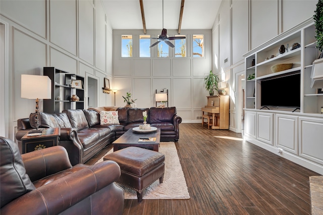 living area with a decorative wall, a high ceiling, a ceiling fan, beamed ceiling, and dark wood finished floors