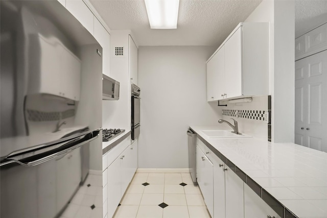 kitchen with tile countertops, appliances with stainless steel finishes, white cabinetry, and a sink