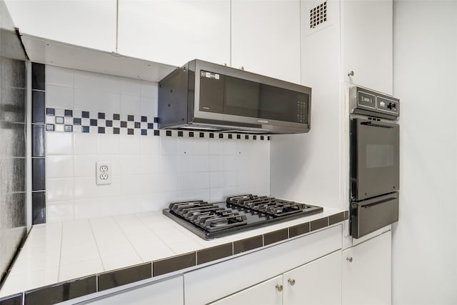 kitchen with tile countertops, visible vents, appliances with stainless steel finishes, white cabinetry, and a warming drawer