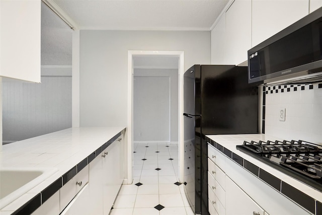 kitchen with black gas cooktop, stainless steel microwave, tasteful backsplash, white cabinets, and tile counters