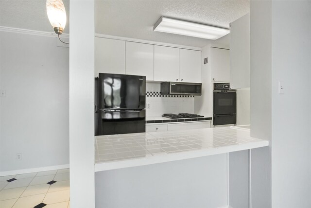 kitchen featuring tile countertops, a peninsula, white cabinets, a textured ceiling, and black appliances