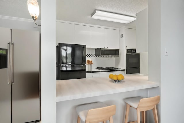 kitchen featuring a breakfast bar area, black appliances, a textured ceiling, white cabinetry, and a warming drawer