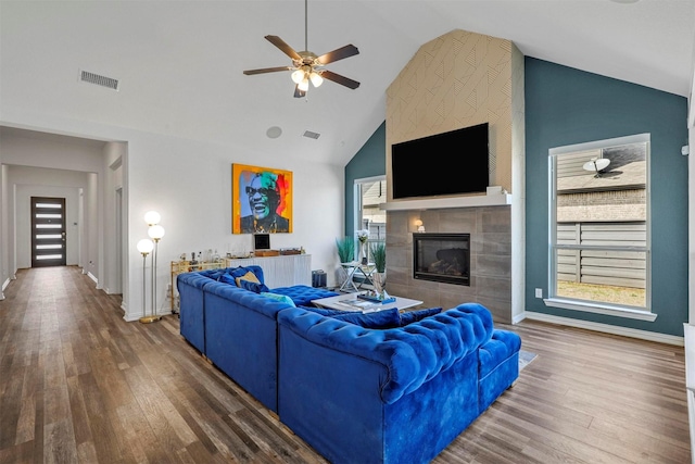 living room featuring wood finished floors, a tile fireplace, visible vents, and baseboards