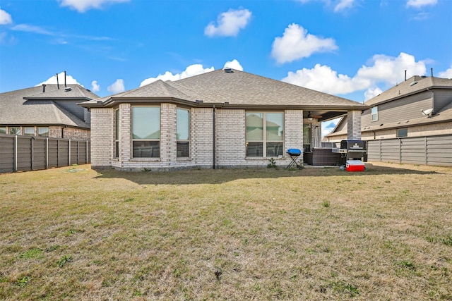 back of house featuring a fenced backyard, a lawn, brick siding, and roof with shingles