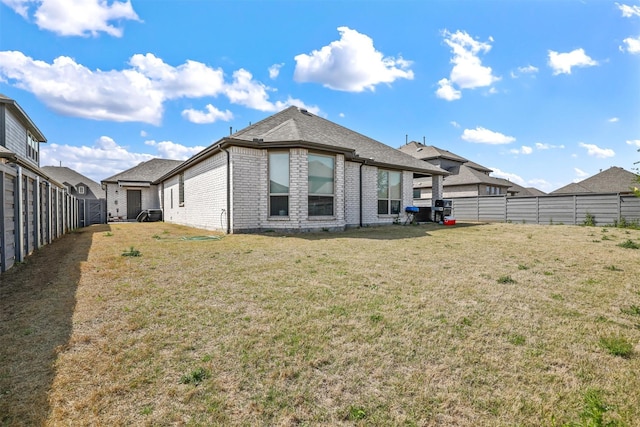 back of property with brick siding, a fenced backyard, roof with shingles, and a yard