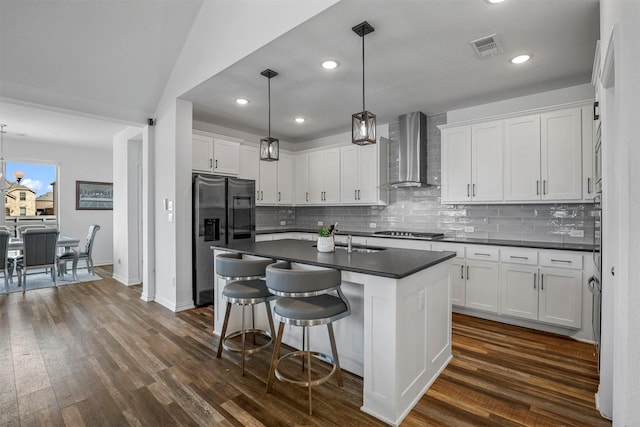 kitchen with dark wood-type flooring, white cabinets, wall chimney range hood, appliances with stainless steel finishes, and dark countertops