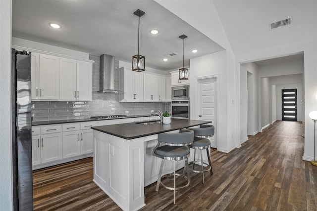 kitchen featuring stainless steel appliances, dark countertops, visible vents, dark wood-type flooring, and wall chimney exhaust hood