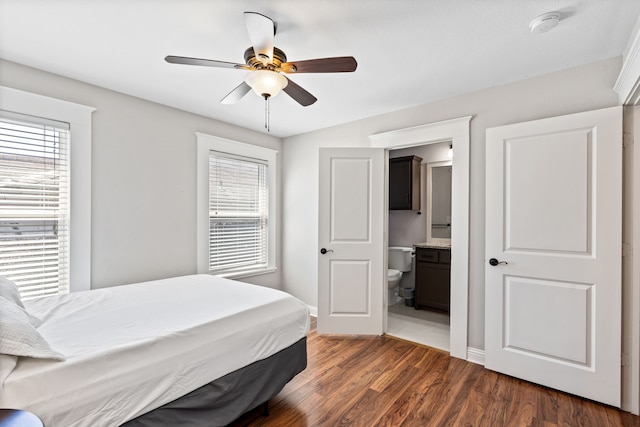 bedroom with ceiling fan, dark wood-type flooring, multiple windows, and connected bathroom