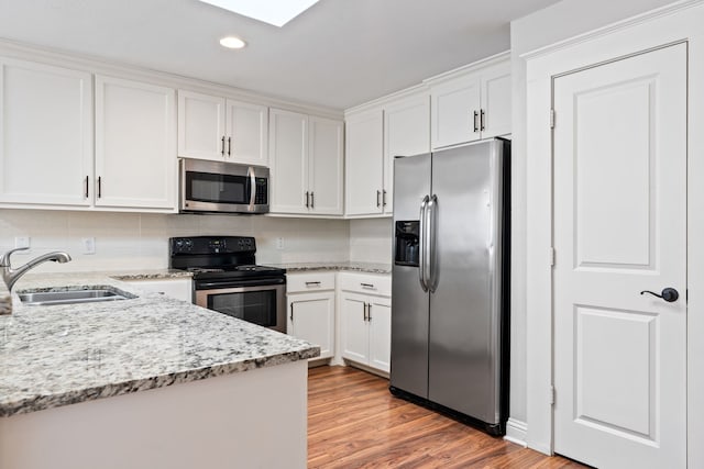 kitchen featuring a sink, light wood-style floors, appliances with stainless steel finishes, white cabinets, and decorative backsplash