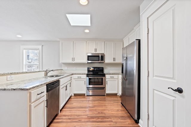 kitchen with light wood-style flooring, a sink, white cabinetry, appliances with stainless steel finishes, and a skylight