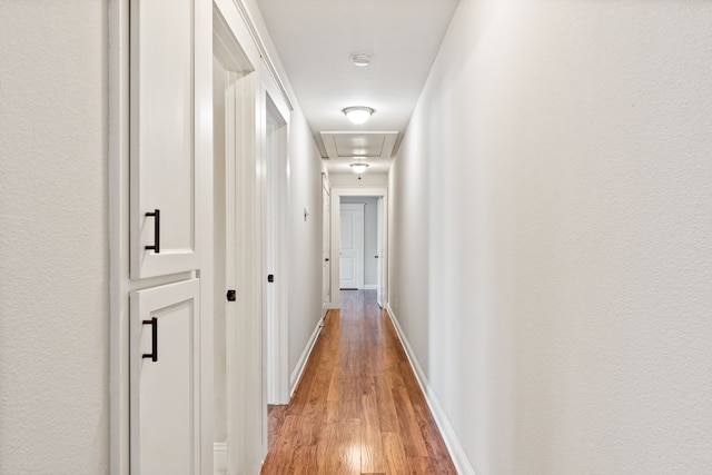 corridor with baseboards, attic access, and light wood-style flooring