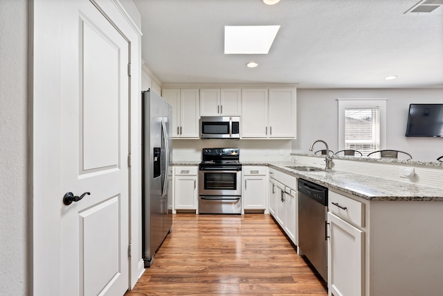 kitchen with visible vents, a sink, a peninsula, appliances with stainless steel finishes, and a skylight