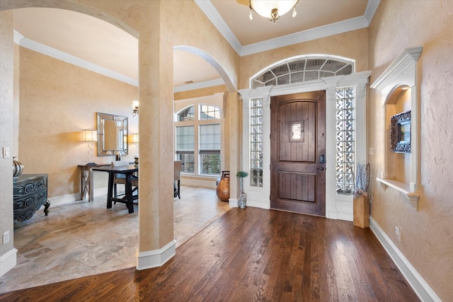 entryway with ornamental molding, wood-type flooring, a towering ceiling, and baseboards