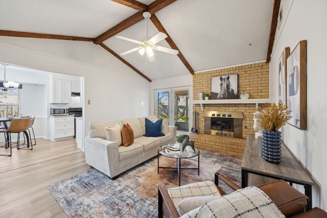 living room featuring vaulted ceiling with beams, a textured ceiling, ceiling fan with notable chandelier, a fireplace, and light wood-type flooring