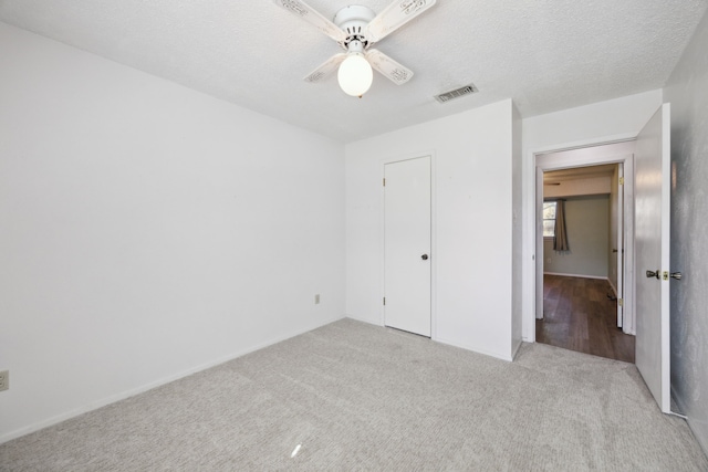 unfurnished bedroom featuring a ceiling fan, visible vents, light carpet, and a textured ceiling