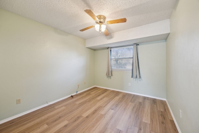 empty room with a textured ceiling, ceiling fan, light wood finished floors, and baseboards