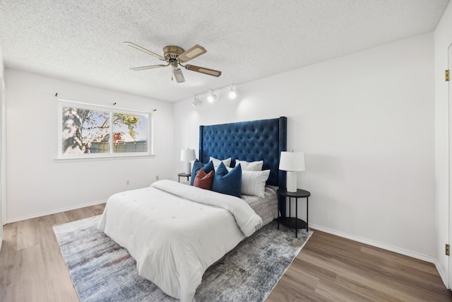 bedroom with ceiling fan, a textured ceiling, baseboards, and wood finished floors