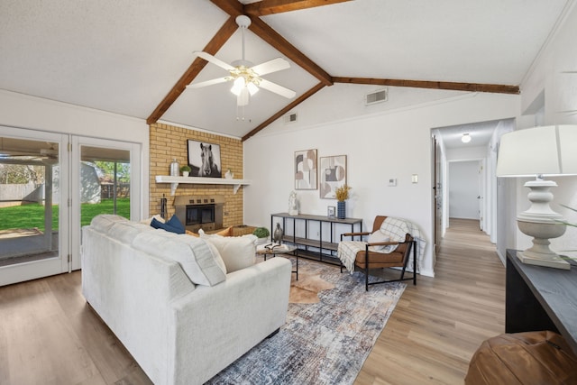 living room featuring light wood-style floors, visible vents, a fireplace, and lofted ceiling with beams