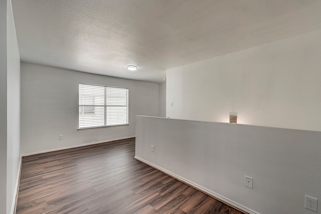 unfurnished room with baseboards, dark wood-type flooring, and a textured ceiling