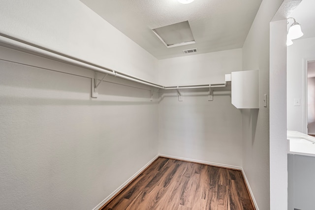 walk in closet with visible vents, attic access, and wood finished floors