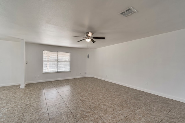 tiled empty room with visible vents, a textured ceiling, baseboards, and a ceiling fan