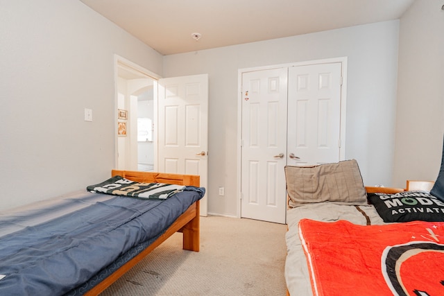 bedroom featuring arched walkways, a closet, baseboards, and light colored carpet