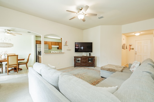 living room featuring light carpet, baseboards, visible vents, arched walkways, and a ceiling fan