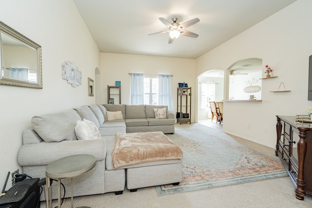 carpeted living area with lofted ceiling, ceiling fan, arched walkways, and baseboards