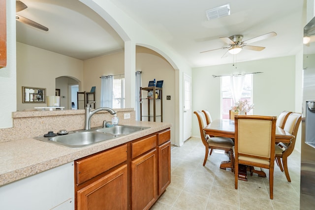 kitchen with arched walkways, visible vents, brown cabinets, light countertops, and a sink