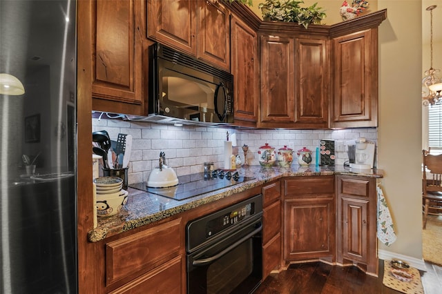 kitchen with dark wood-type flooring, baseboards, dark stone counters, decorative backsplash, and black appliances